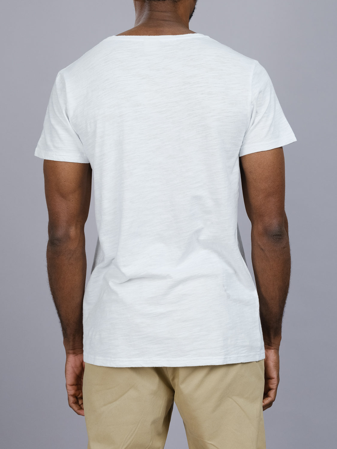 A person is photographed from behind in a casual look, wearing the ID Menswear Mini Flip Slub Yarn Tee in white and beige pants against a gray background.