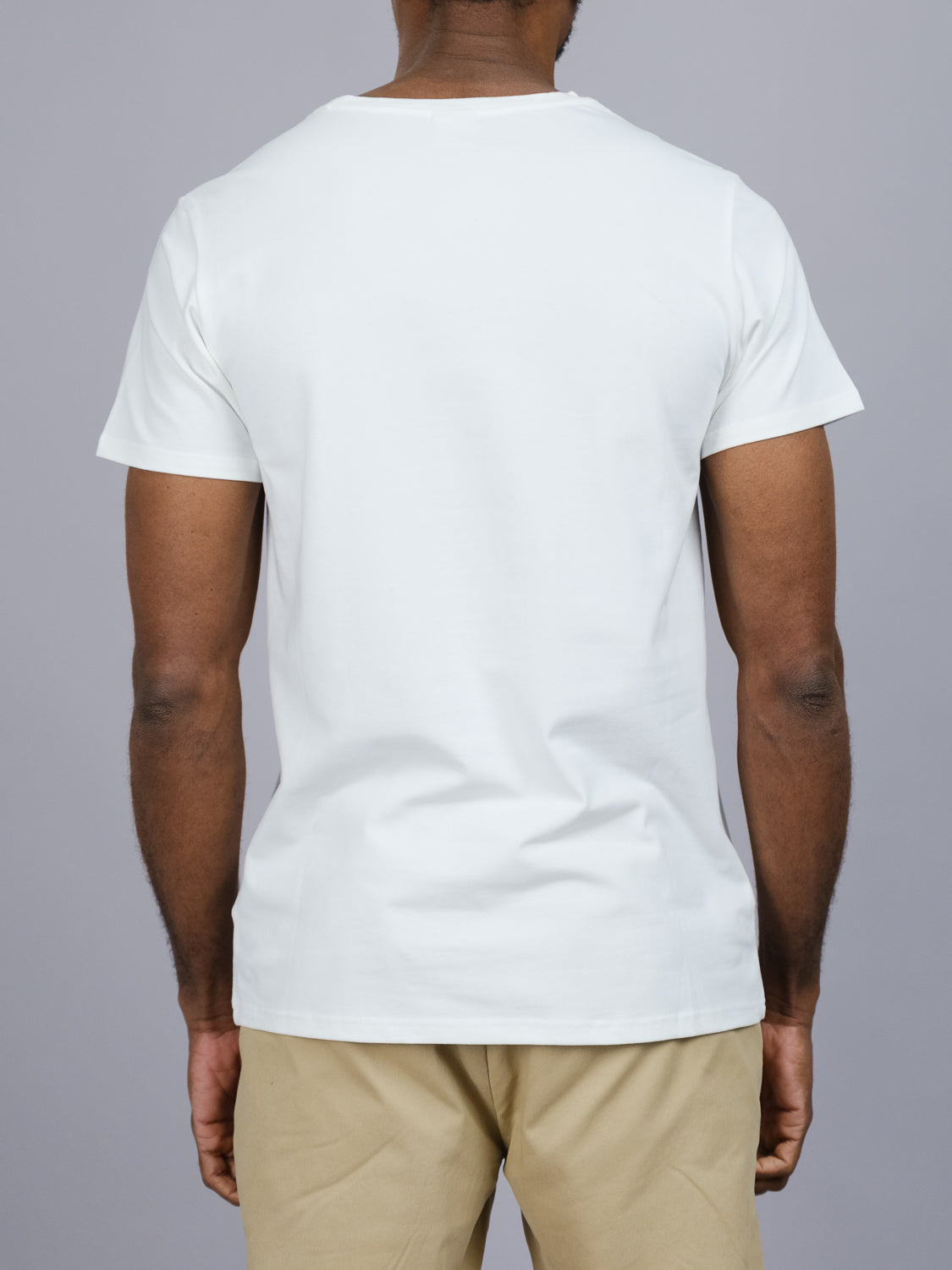 A person wearing the Form Crew Neck Tee by ID Menswear, which is a form-fitting white t-shirt paired with beige pants made from comfortable fabric, is shown from the back against a gray background.