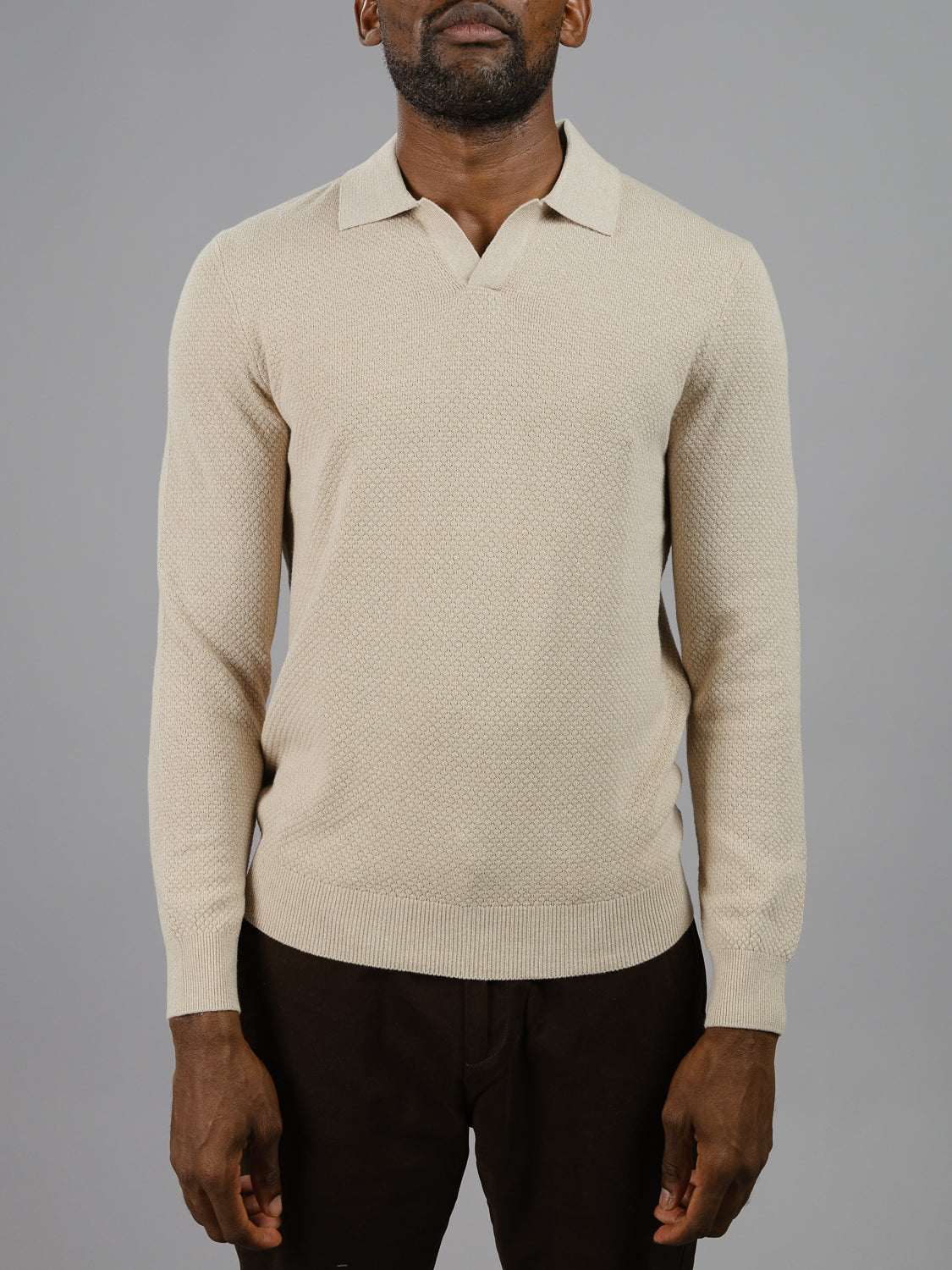 A man stands against a plain gray background wearing ID Menswears Seattle Long Sleeve Cotton Polo, exuding effortless style in beige cotton with dark pants, perfect for smart-casual occasions.
