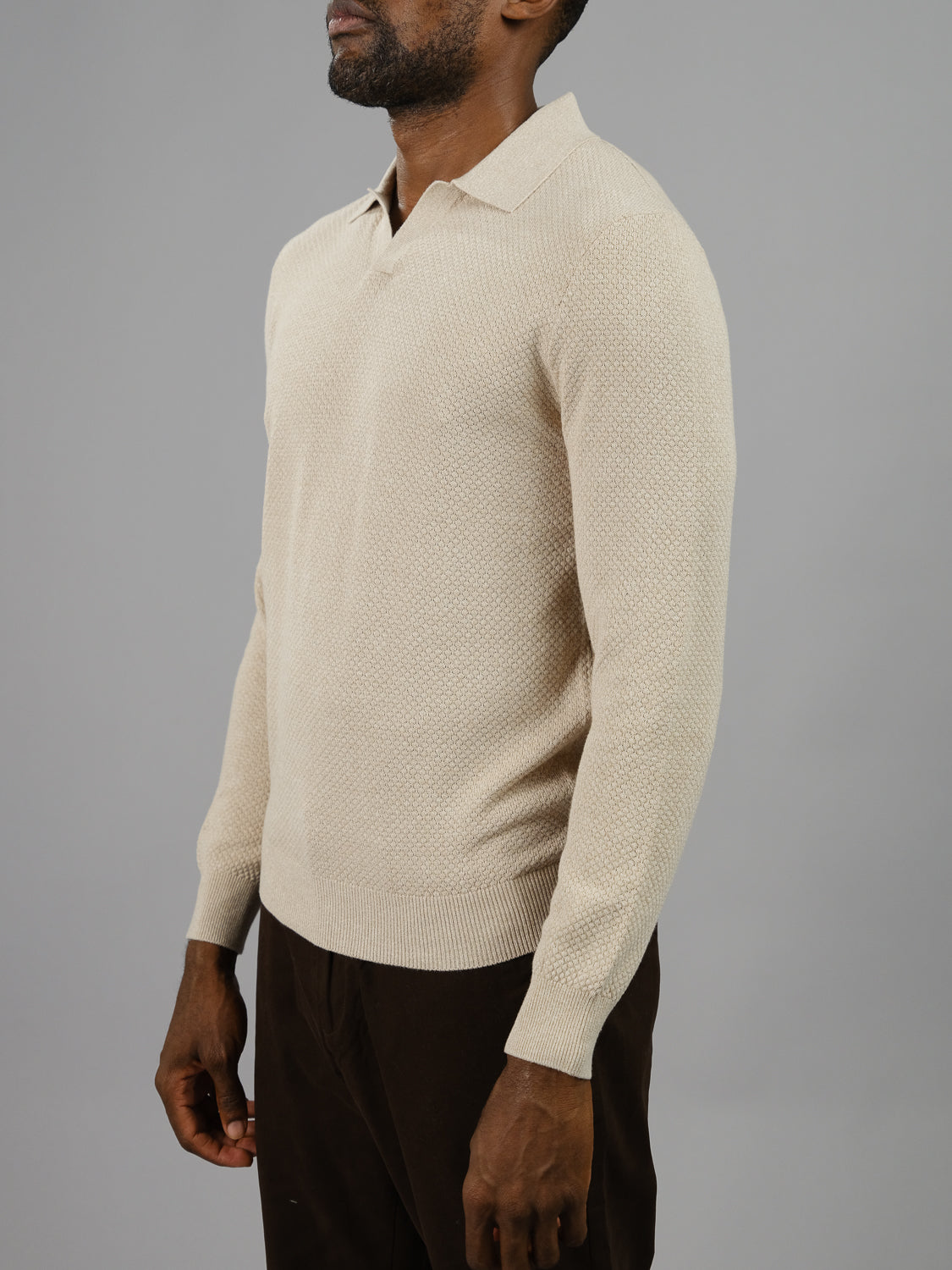 A man embodies smart-casual style in the ID Menswear Seattle Long Sleeve Cotton Polo, a light beige collared knit sweater, against a gray background. Paired with dark brown pants, its perfect for Seattles laid-back charm and brisk evenings.