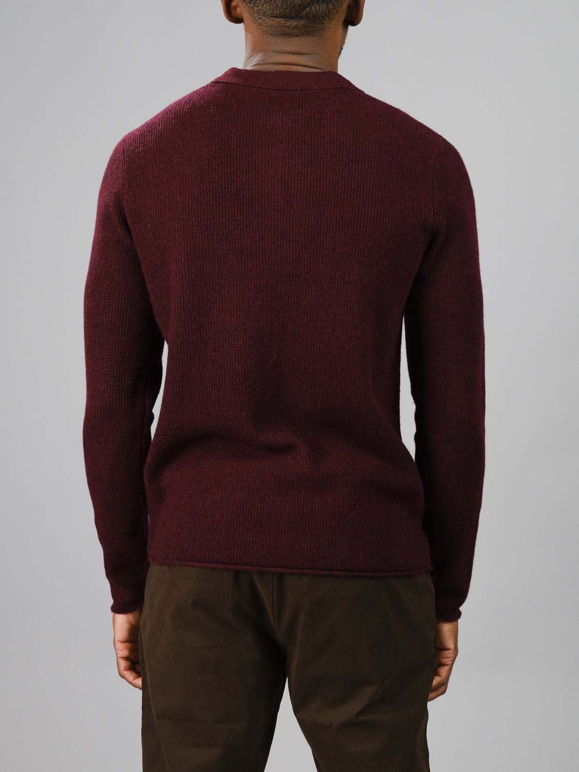 A person showcasing casual elegance is seen from the back, wearing an ID Menswear Gothenberg Merino Sweater Polo and brown pants against a plain gray background.