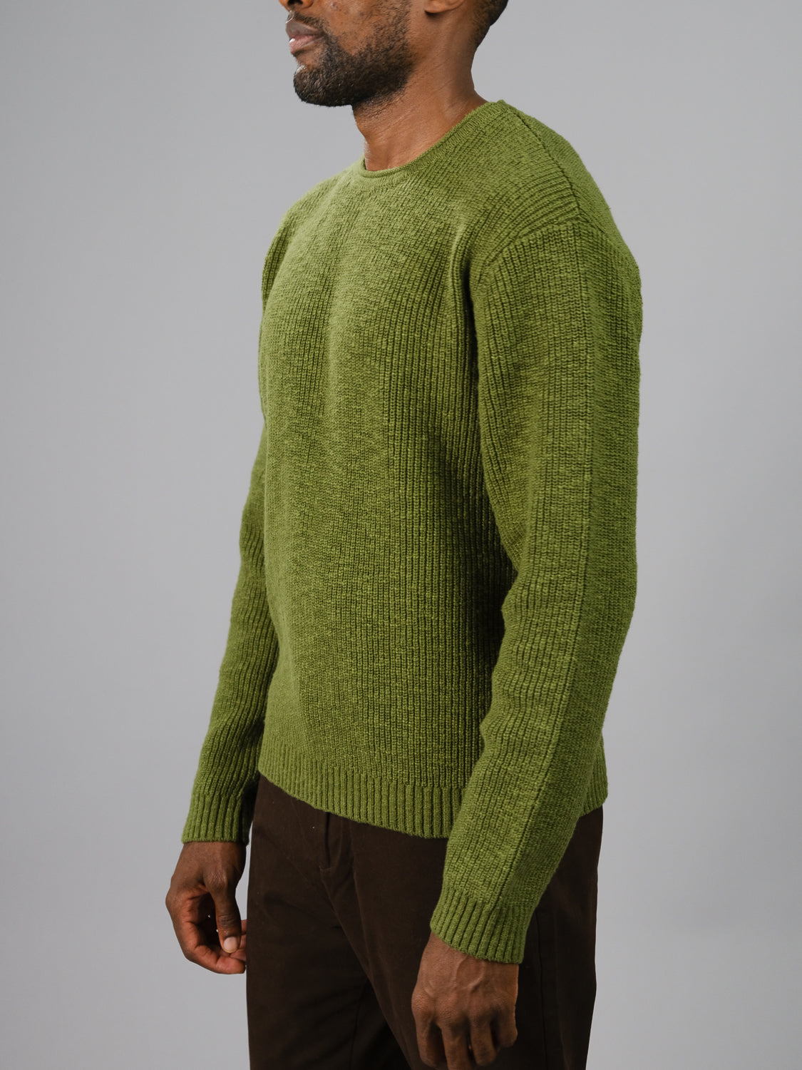 A person in a Dublin Slub Cotton Rolled Neck Sweater by ID Menswear and brown pants stands against a gray backdrop, side view highlighting the slub cotton texture, ideal for cooler days.