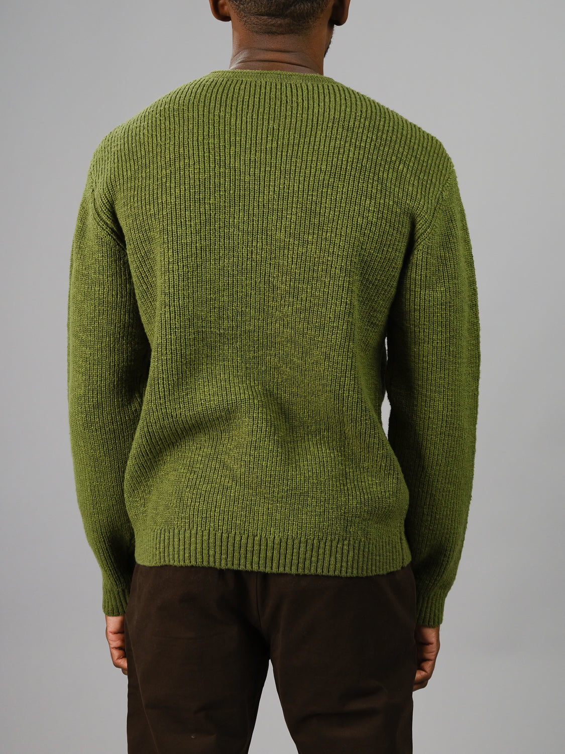 An individual wearing the olive green Dublin Slub Cotton Rolled Neck Sweater by ID Menswear and dark pants faces away, set against a plain gray background.
