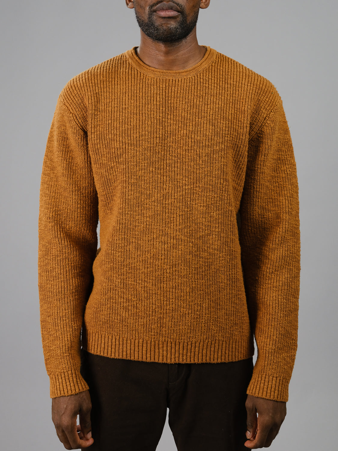 Against a plain gray background, a man models the ID Menswear Dublin Slub Cotton Rolled Neck Sweater, known for its ribbed design and long sleeves ideal for cooler weather. He pairs it with dark pants, and the photo elegantly captures his upper body.