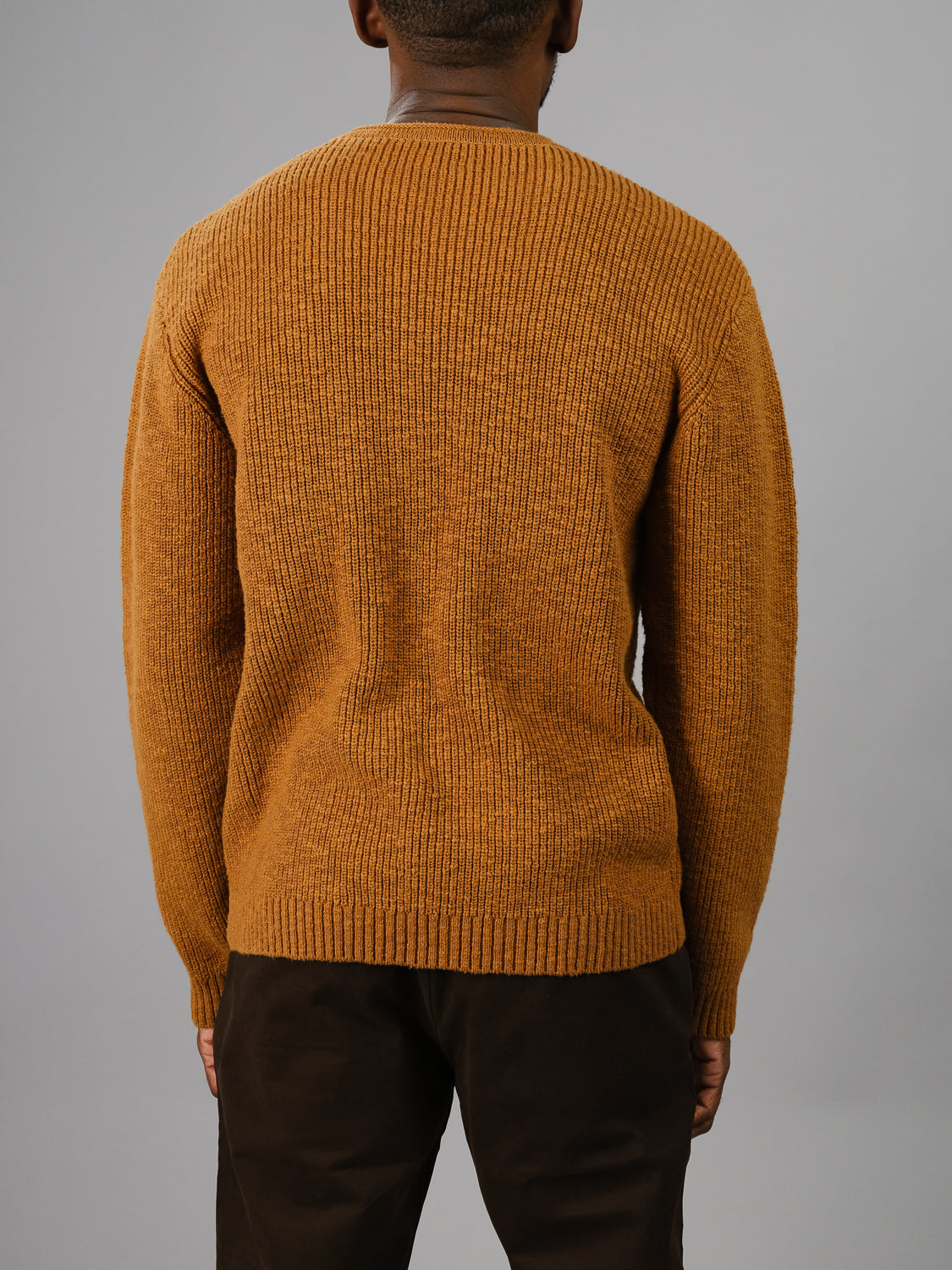 Against a plain gray background, a person wears dark pants and the ID Menswear Dublin Slub Cotton Rolled Neck Sweater in textured brown, ideal for cooler weather.