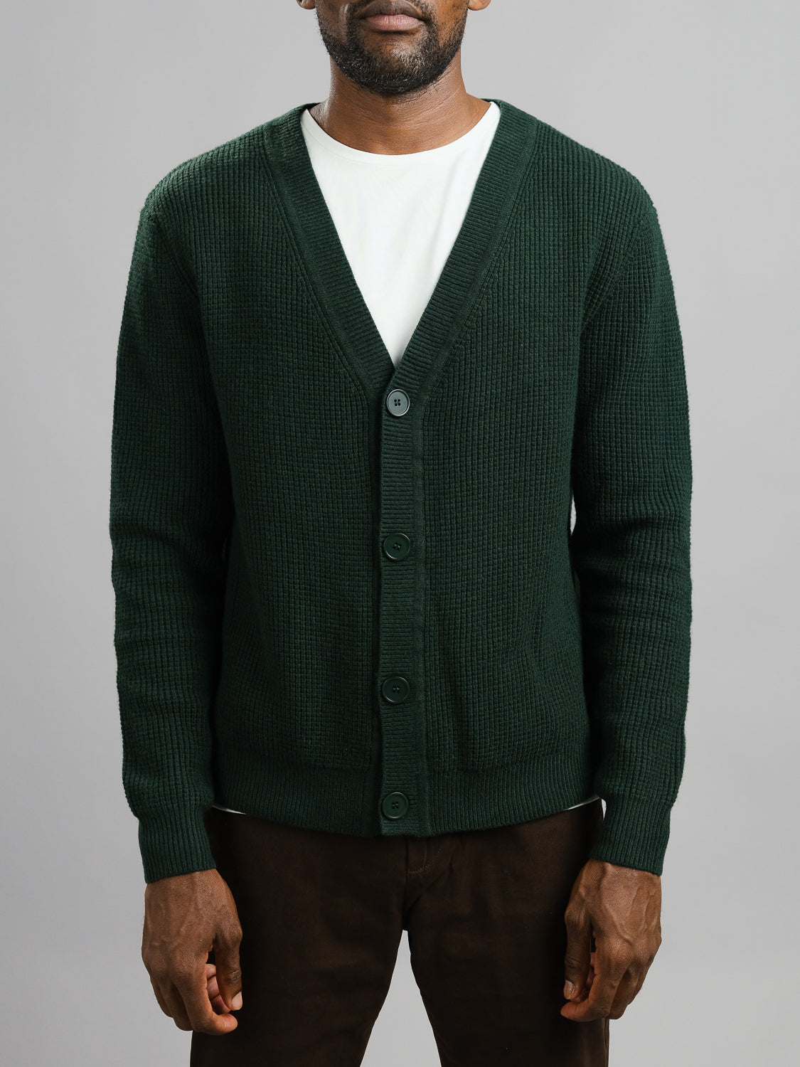 A person wears the Dundee Waffle Knit Merino Cardigan by ID Menswear over a white T-shirt and brown pants, standing against a plain gray background with their face partially out of frame.