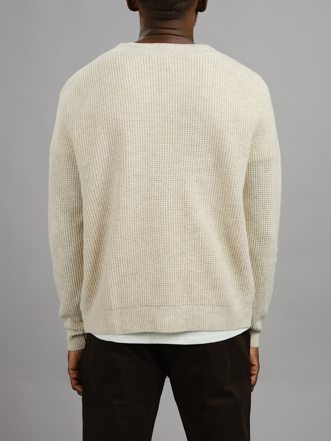 A person is shown from behind wearing the ID Menswear Dundee Waffle Knit Merino Cardigan in cream and dark pants, standing against a plain gray background.