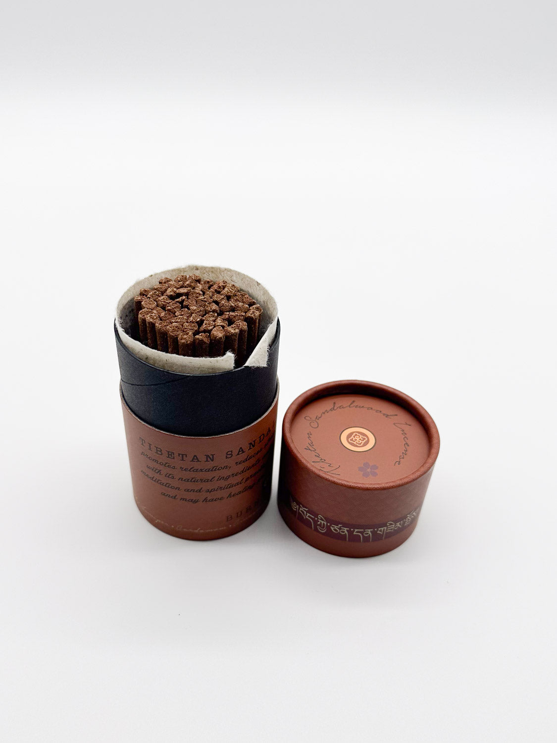A cylindrical ID Menswear container of Tibetan Sandalwood Incense, ideal for meditation and relaxation, features decorative text and symbols on a white background. Removing the lid unveils the soothing aroma.