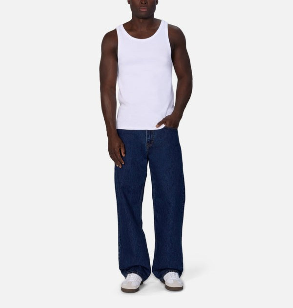 Wearing the Industrie Washed Brando Ribbed Tank Top with loose dark blue jeans and white sneakers against a plain light background creates an ideal summer look for your wardrobe.