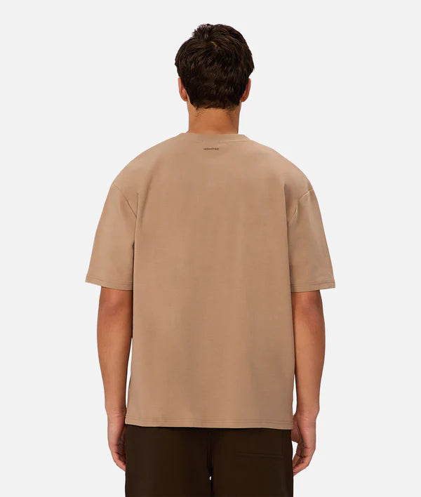 A person with short dark hair is seen from behind, wearing Industrie’s loose-fitting, 90s-inspired The Newport T-Shirt and dark pants, standing against a plain white background.