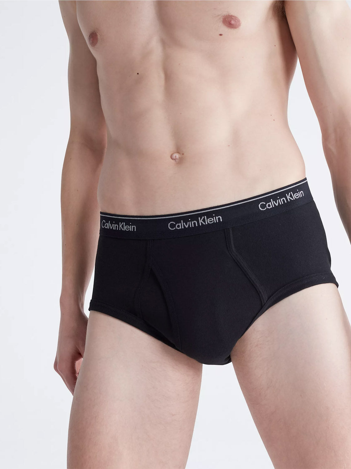 A person wearing Calvin Klein NB3999 3-Pack Classic Cotton Briefs in black, shown from mid-chest to upper thighs, stands against a plain light background.