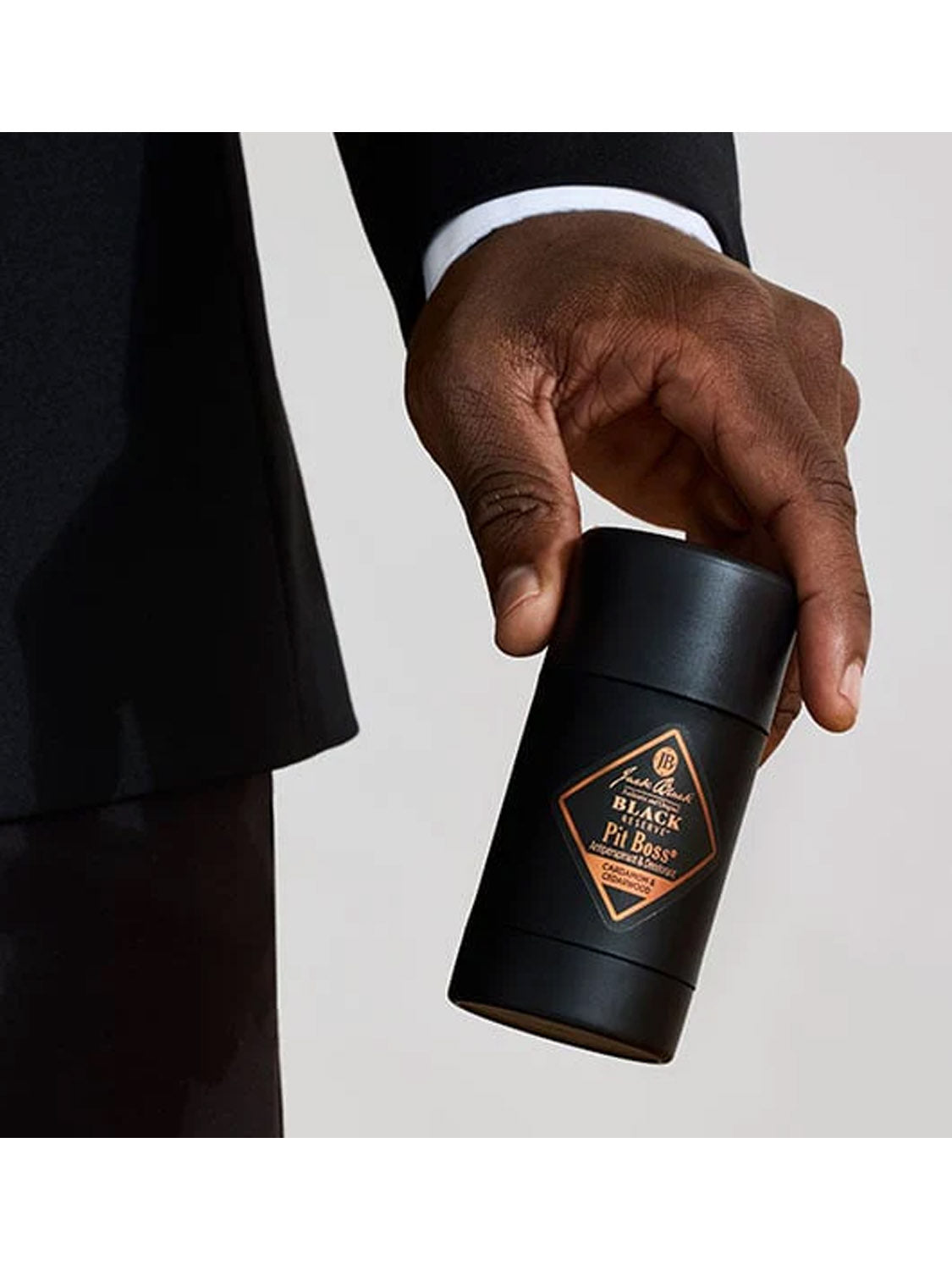 A person in a black suit holds a black cylindrical container labeled Jack Black Black Reserve™ Pit Boss® Antiperspirant & Deodorant against a plain light background.