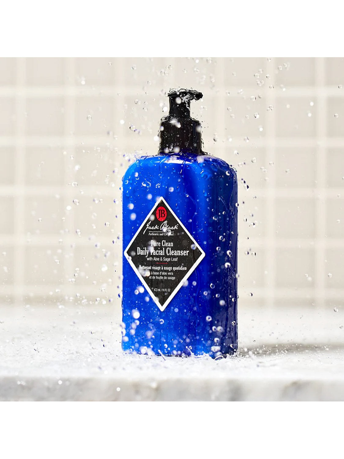 A 6 oz blue pump bottle of Jack Black Pure Clean Daily Facial Cleanser sits on a wet surface with splashing water droplets, set against a tiled background.