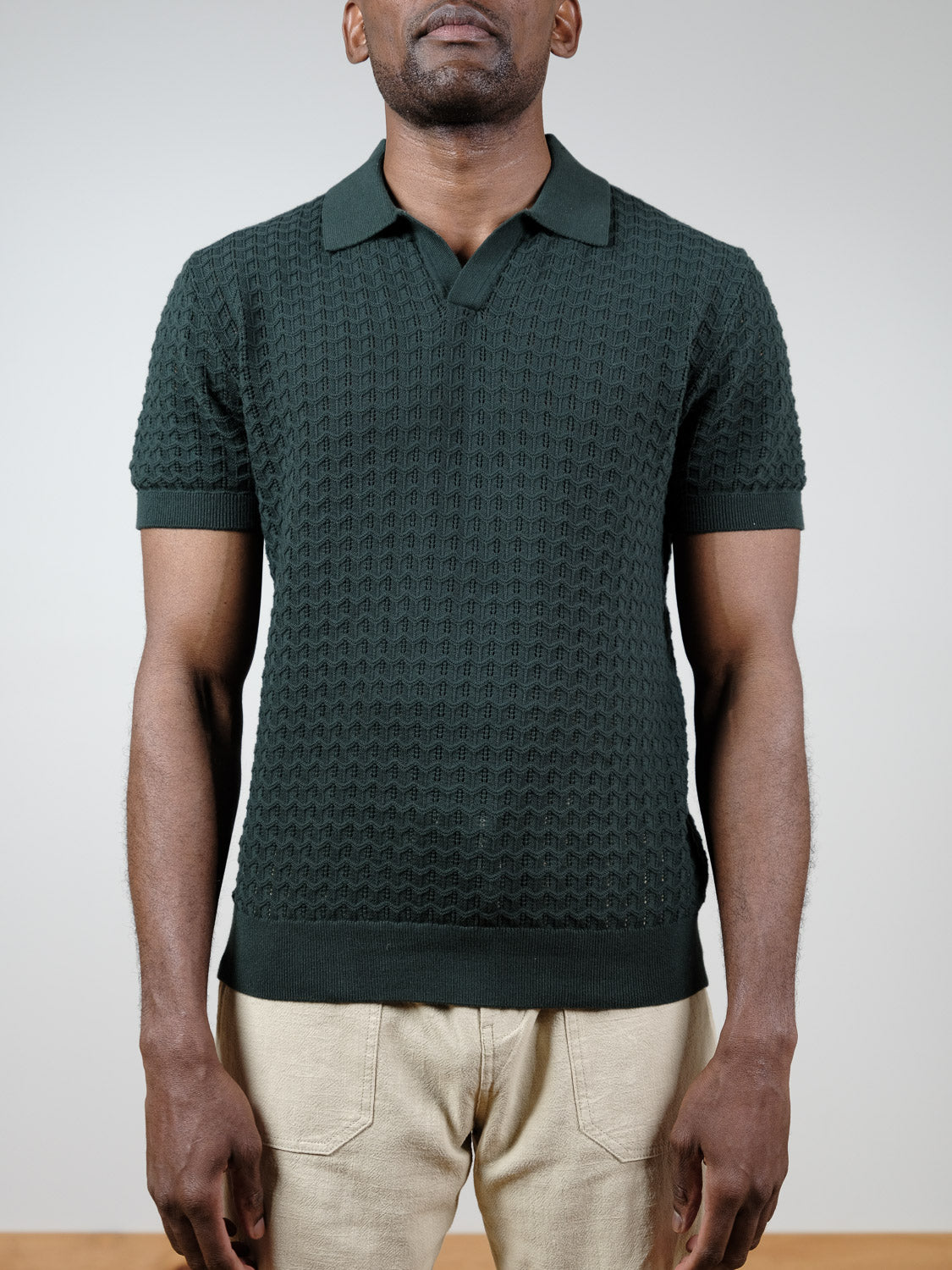 A man stands facing forward against a light gray background, wearing the Mojave Knitted Cotton Polo by ID Menswear and beige pants. His face is partially out of frame, focusing attention on this classic casual staple.