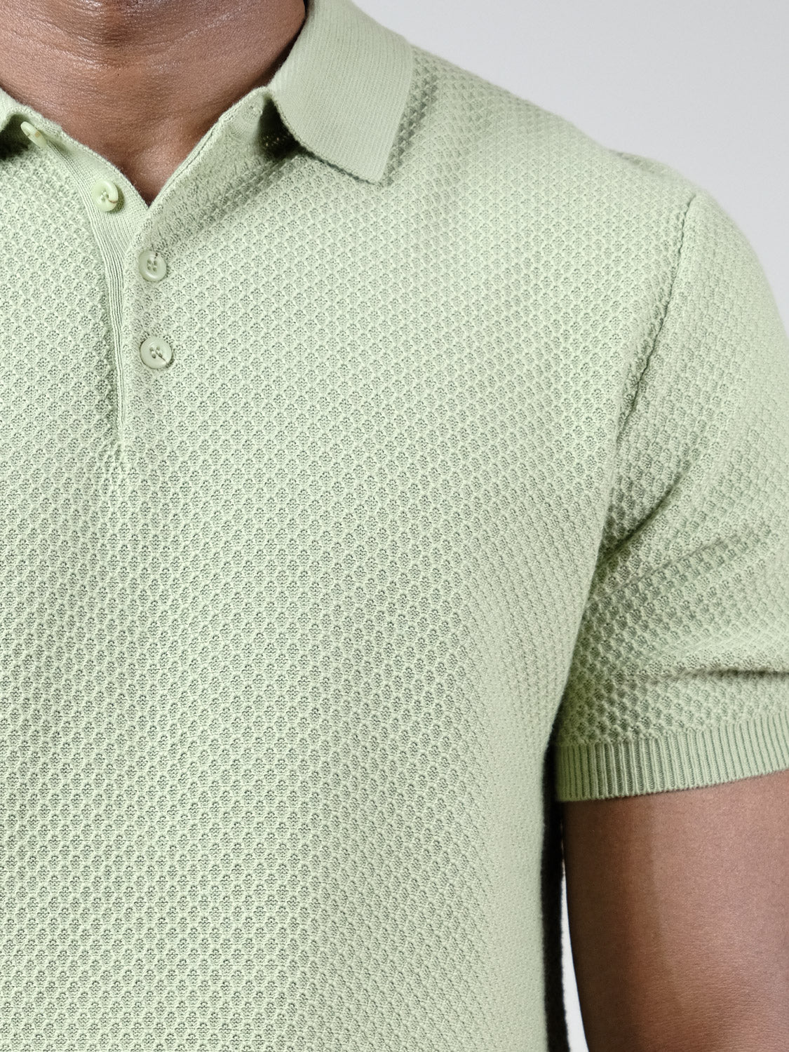 A close-up shows a person wearing the Tucson Knitted Cotton Polo by ID Menswear in light green, featuring a textured cotton-knit, classic collar, and buttons. The focus highlights its premium, breathable design on the upper torso.