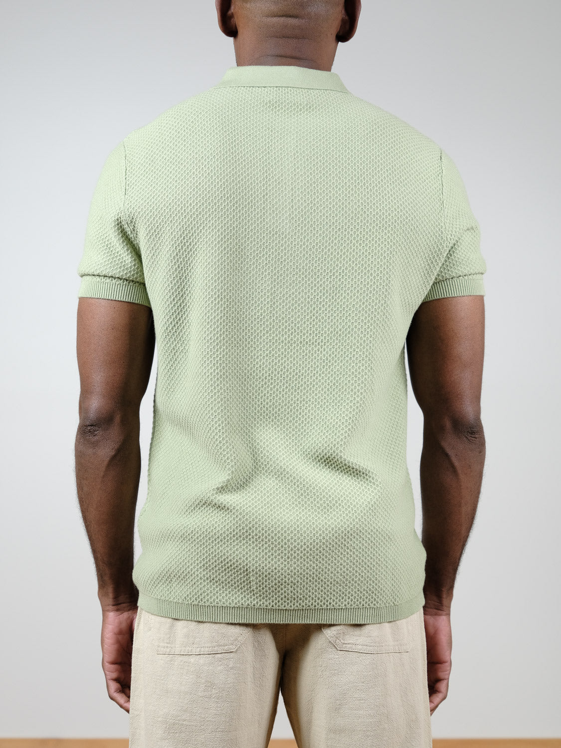 A person is seen from behind wearing the Tucson Knitted Cotton Polo in light green by ID Menswear with beige pants, set against a plain, neutral background.