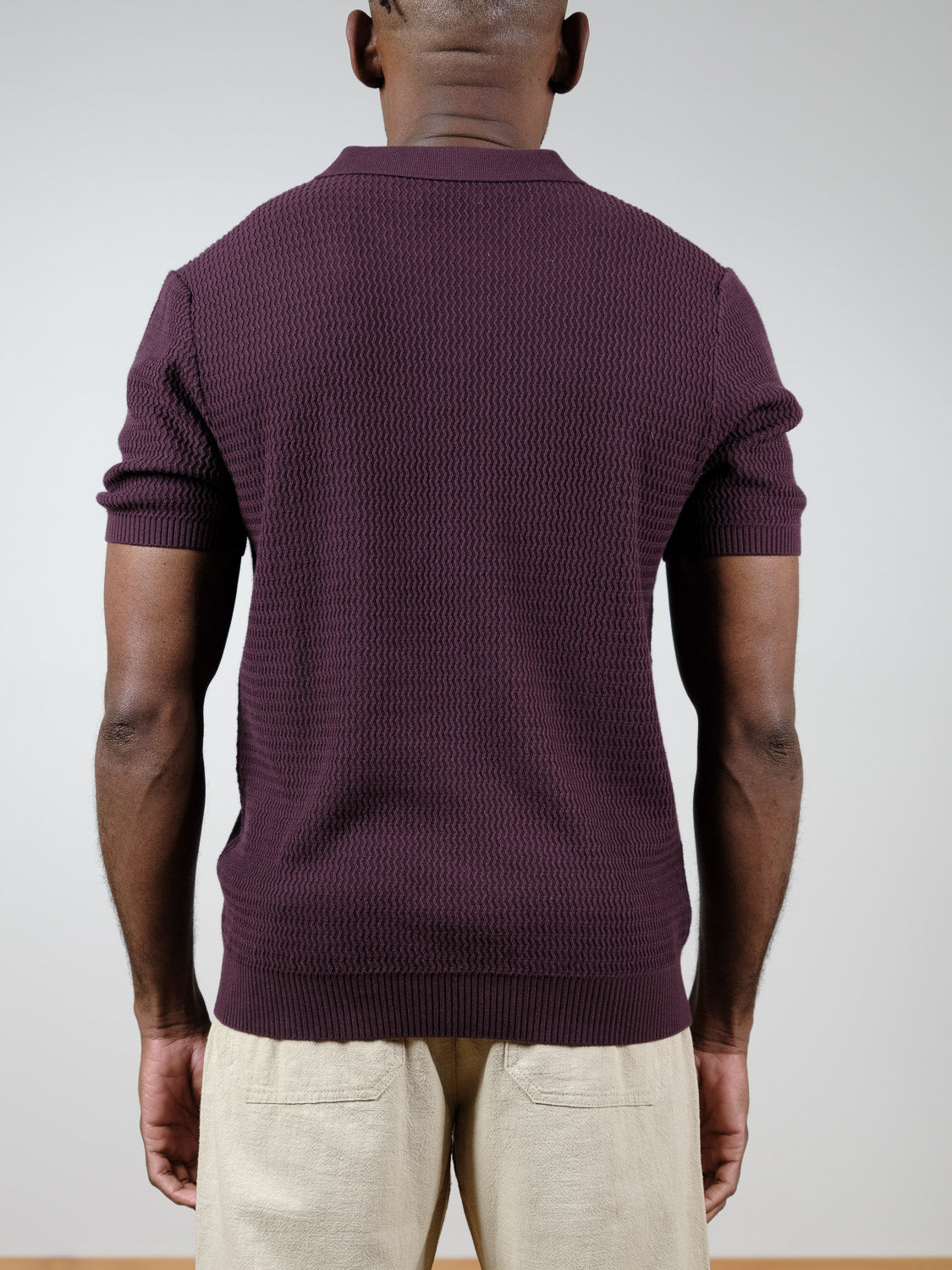 A person is standing with their back to the camera, wearing the Mecca Knitted Cotton Polo by ID Menswear and light beige pants against a plain background.