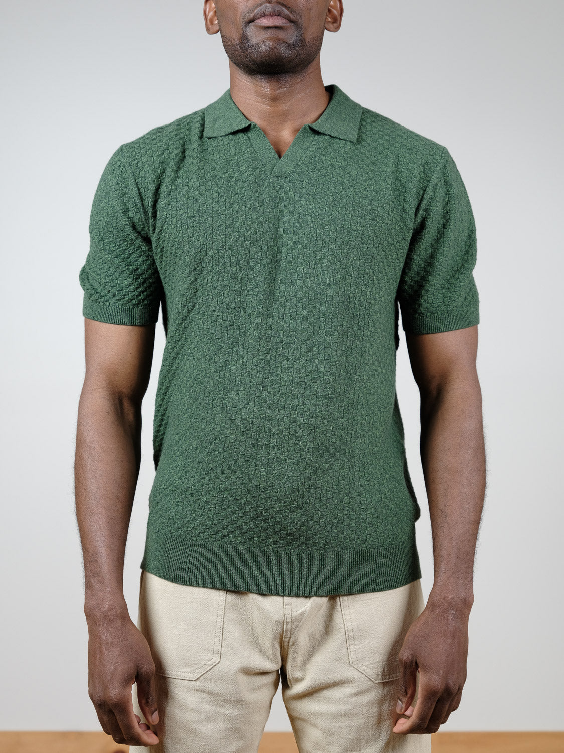 A man models the Cairo Knitted Cotton Polo by ID Menswear in textured green cotton, paired with beige pants, standing against a plain light background and displaying breathable premium casual wear.