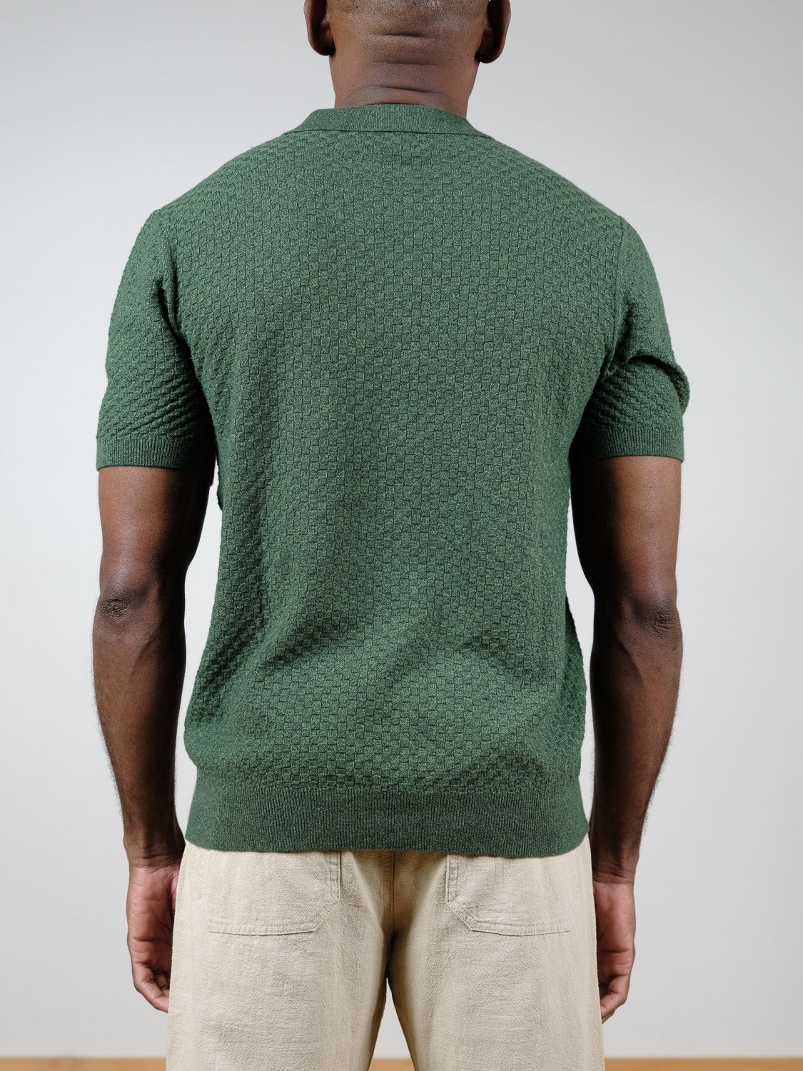 A person wears the ID Menswear Cairo Knitted Cotton Polo in green with light beige pants, facing away from the camera against a plain background, showcasing premium casual style.