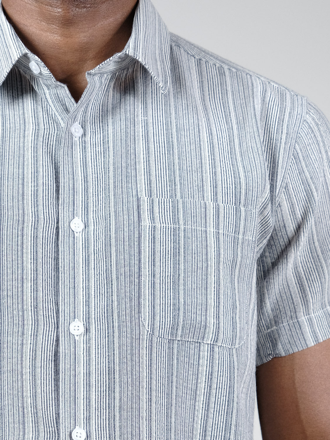 Close-up of a person wearing the Strider Short Sleeve Shirt by ID Menswear. This relaxed fit, button-down has vertical blue and white stripes, a left chest pocket, and is crafted from breathable cotton. Only the torso and neck are visible.
