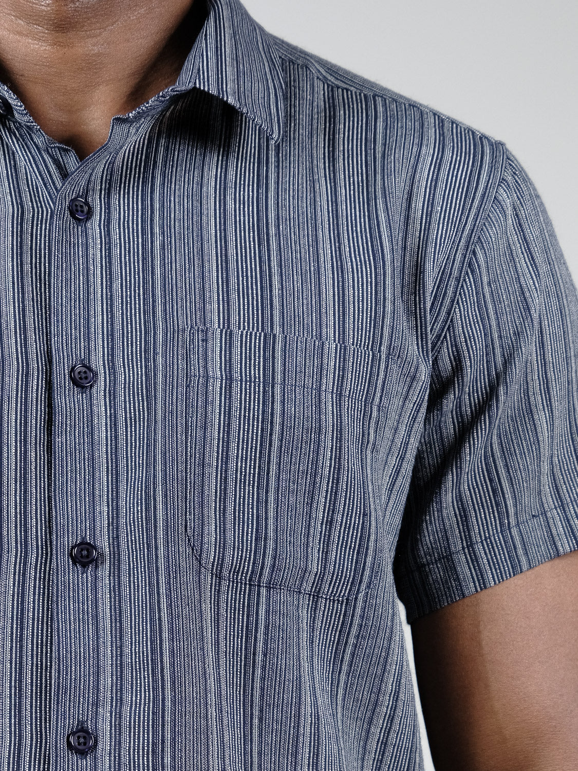 Close-up of a person wearing the ID Menswear Strider Short Sleeve Shirt, featuring breathable cotton and blue and white vertical stripes, with a chest pocket visible from the chest to neck and part of the left arm.