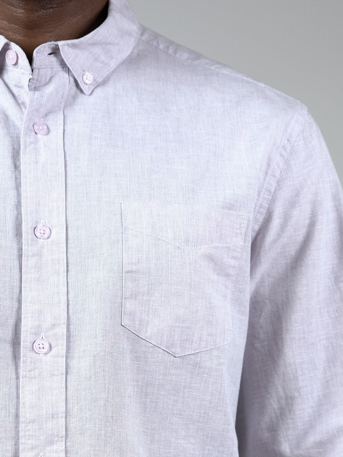 Close-up of a person wearing the Darwin Long Sleeve Shirt by ID Menswear in light purple, relaxed fit with a front pocket; shows the upper torso and part of the neck against a plain gray background.