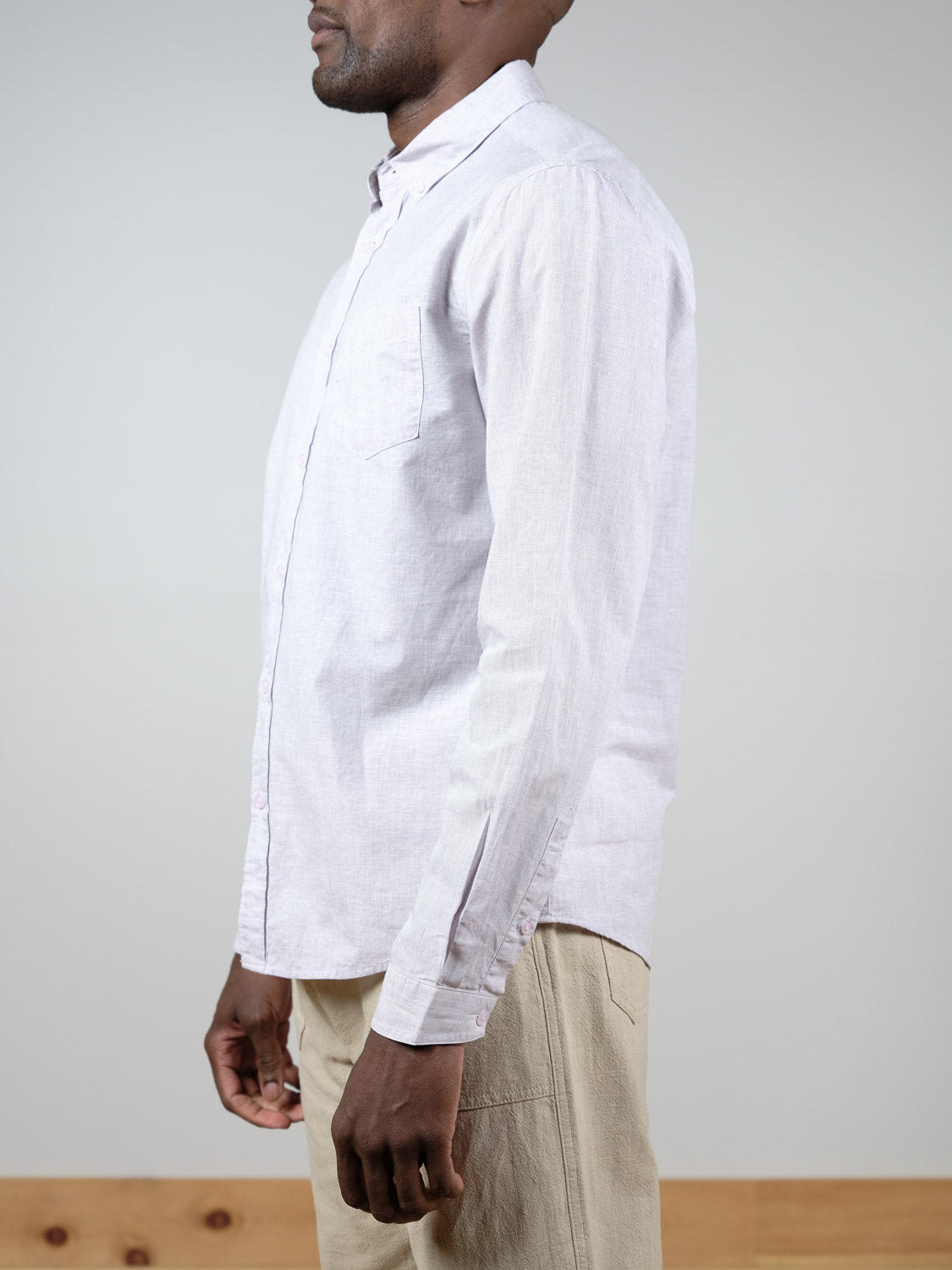 A man stands in profile against a plain background, wearing the light-colored Darwin Long Sleeve Shirt by ID Menswear and beige pants.