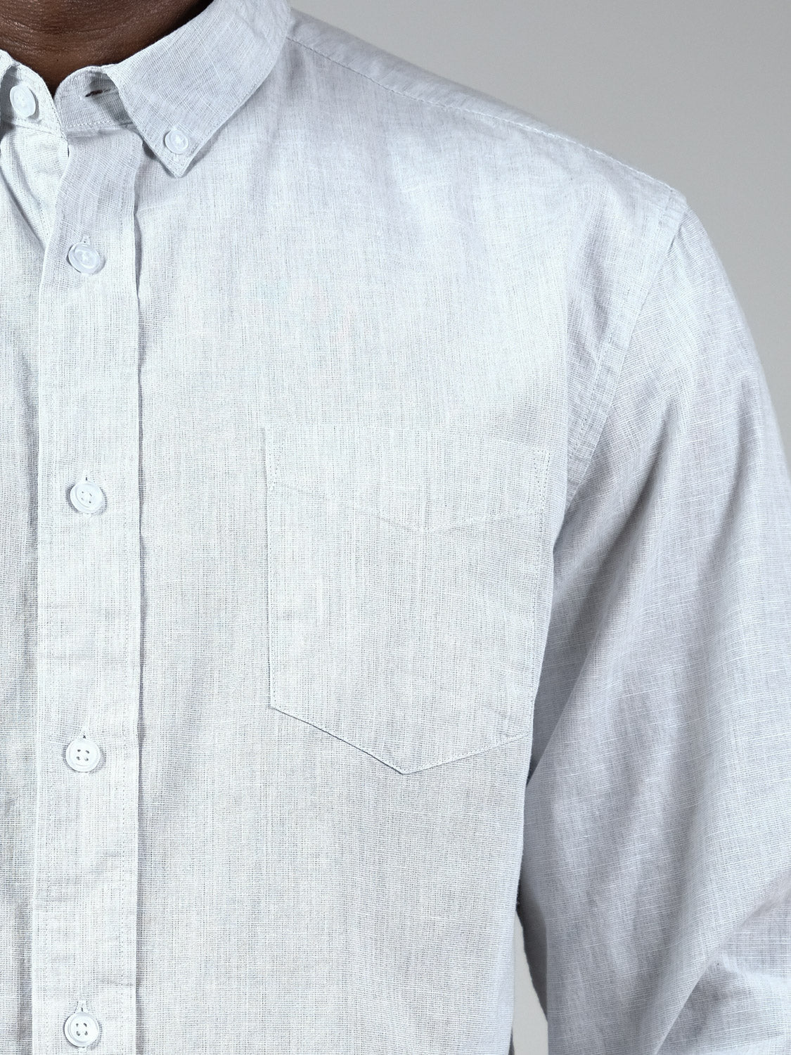 Close-up of a person wearing the Darwin Long Sleeve Shirt by ID Menswear, featuring light gray breathable linen, a pointed collar, and chest pocket. Photographed from shoulders to mid-torso against a plain background.