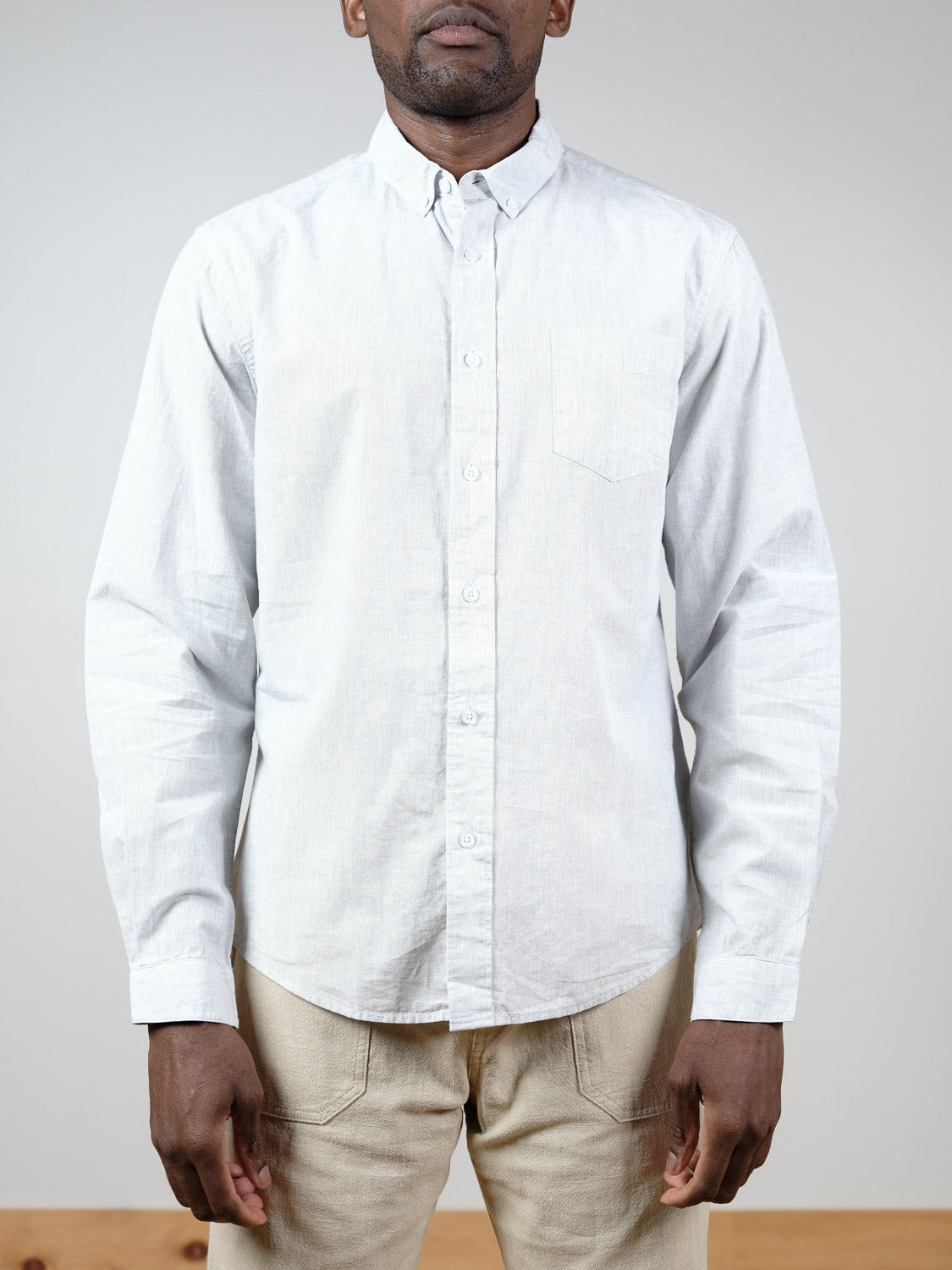 A person models the ID Menswear Darwin Long Sleeve Shirt in light gray, styled with beige pants against a light background. The relaxed fit and casual look are shown as the frame slightly crops out their head.