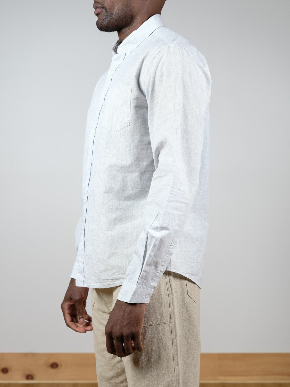 A person stands sideways against a plain background, showing only their upper body while wearing the Darwin Long Sleeve Shirt by ID Menswear in light gray and beige pants.