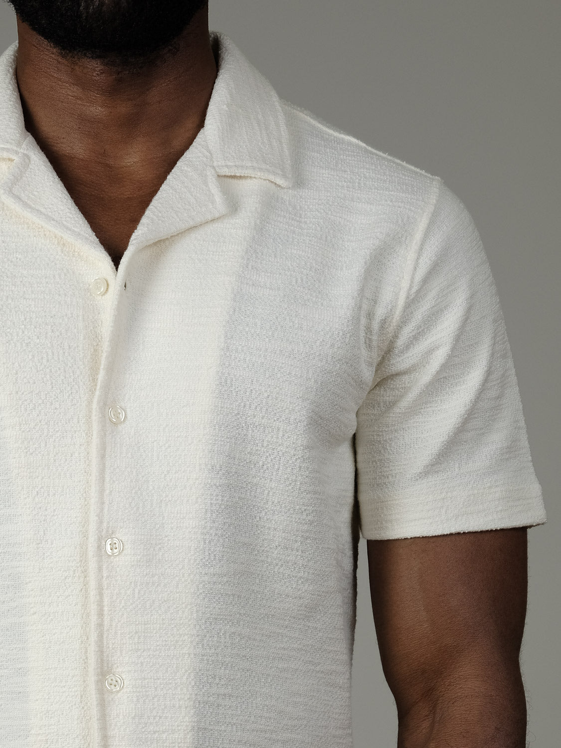 A person wears the Casual Friday Egebjerg Resort Shirt, a cream-colored, lightweight cotton-polyester blend with short sleeves and textured buttons, standing against a plain gray background. Only their upper body and part of their face are visible.