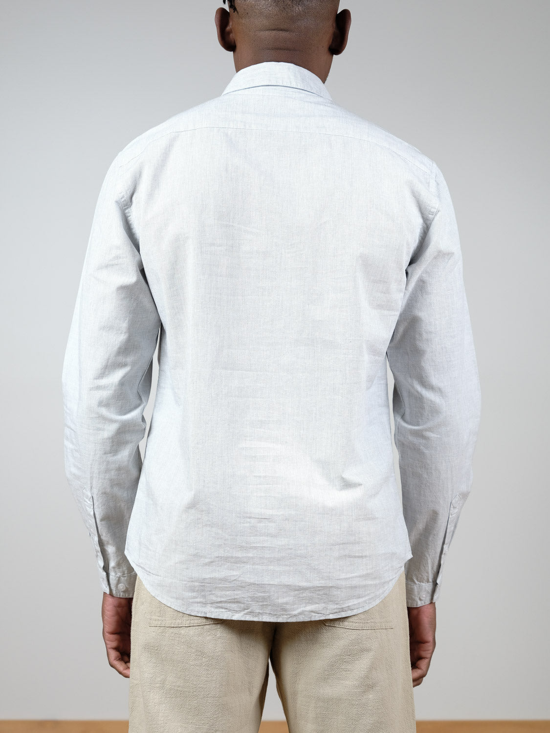 A person faces away from the camera, wearing the Darwin Long Sleeve Shirt in light grey by ID Menswear and light beige pants against a plain, neutral background.