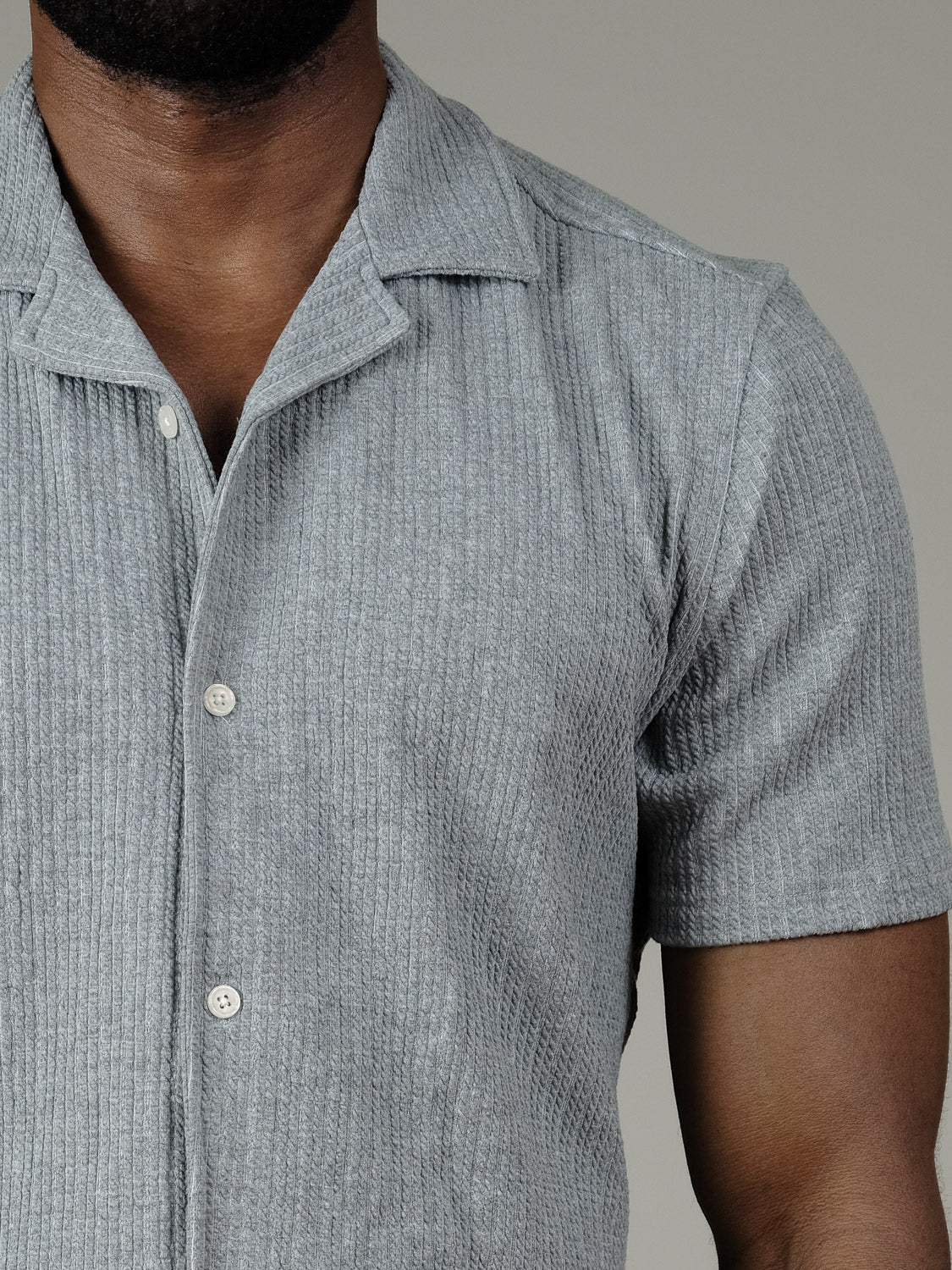 A close-up of a person wearing the Civil Society Viggo Knit Resort Shirt in light gray, featuring short sleeves, a knit texture, and a collar; shown from neck to upper arm against a plain background.