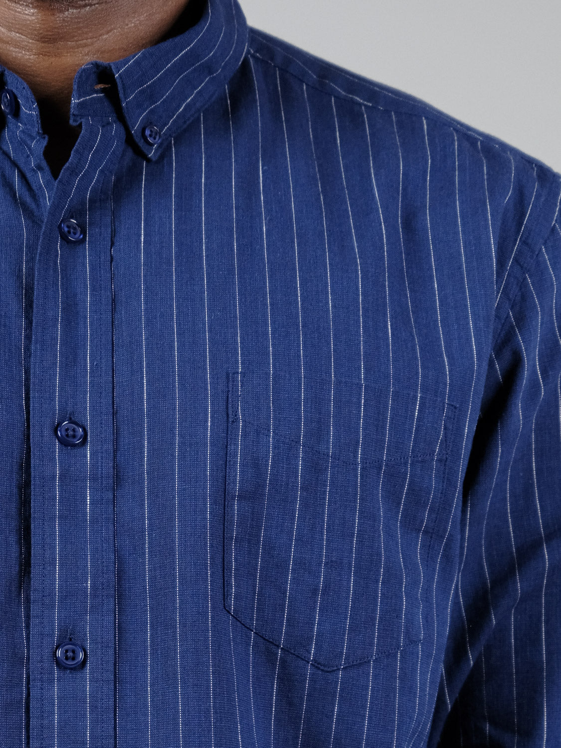 A close-up of a person wearing the ID Menswear Dubai Long Sleeve Shirt—a blue cotton-linen blend with white vertical pinstripes and a chest pocket—showing only the chest and part of the neck.