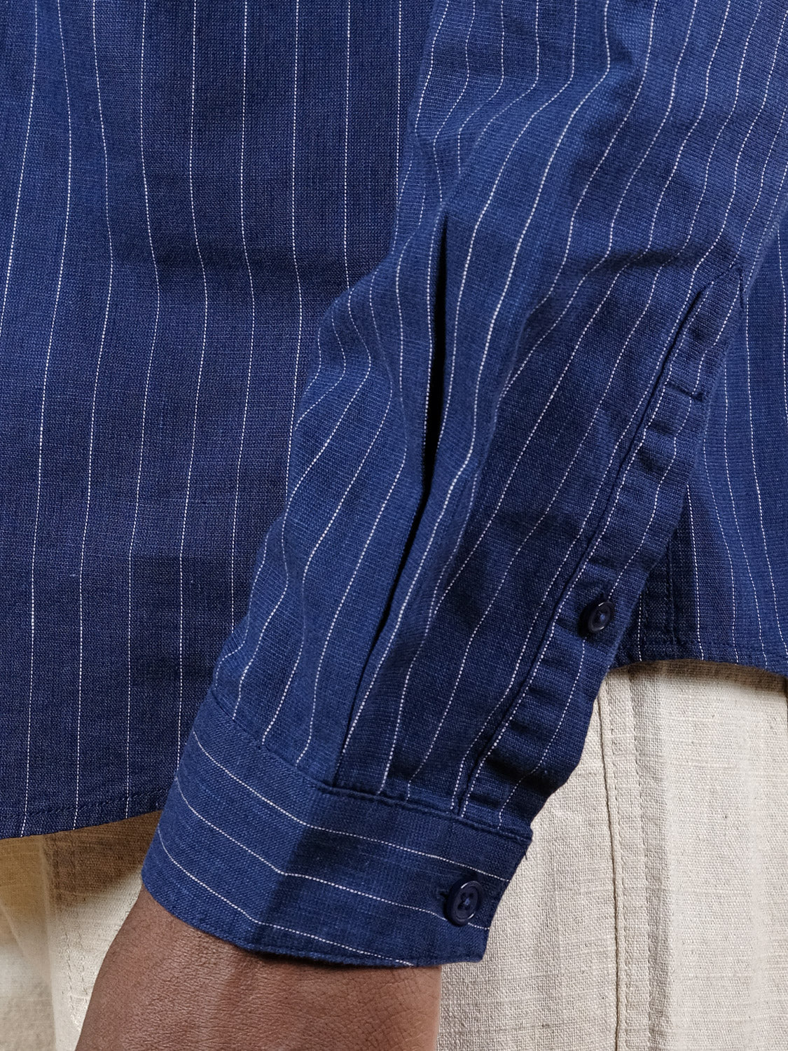 A close-up of a person’s arm in the ID Menswear Dubai Long Sleeve Shirt, featuring a blue, relaxed fit with pinstripes and buttoned cuffs, paired with light pants. The cotton-linen blend stands out against the blurred background.