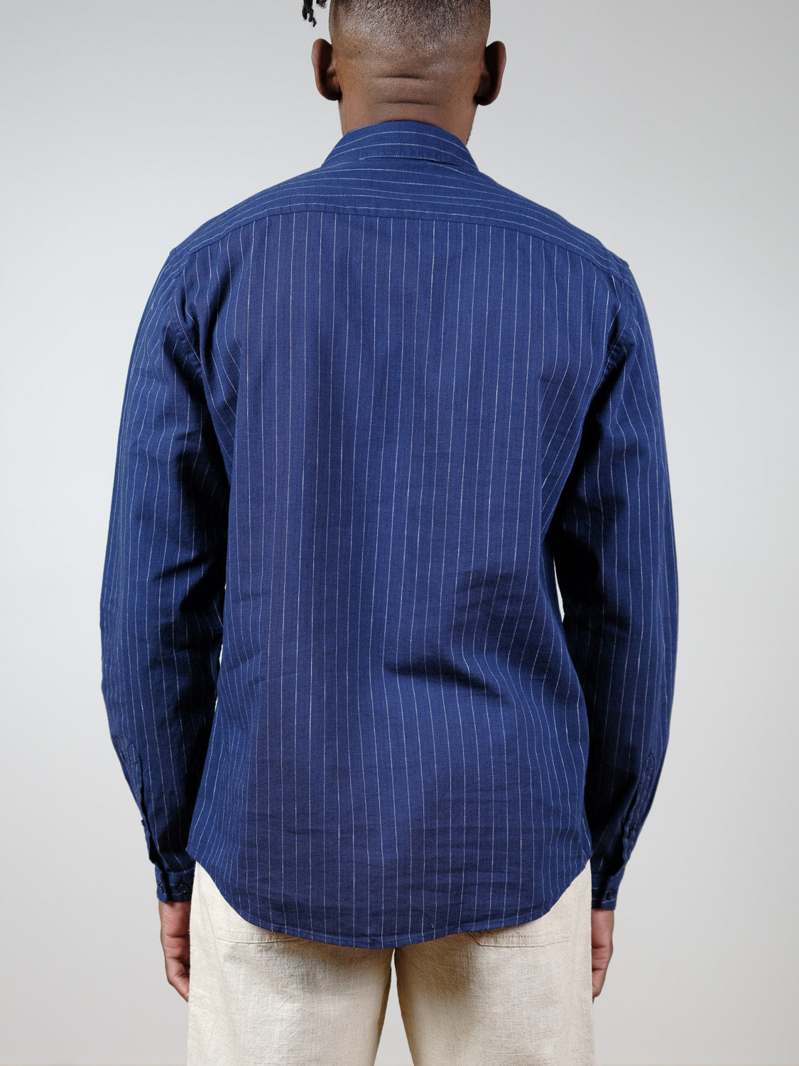 A person faces away from the camera, wearing the navy Dubai Long Sleeve Shirt by ID Menswear in a cotton-linen blend with light pants, set against a plain light background.