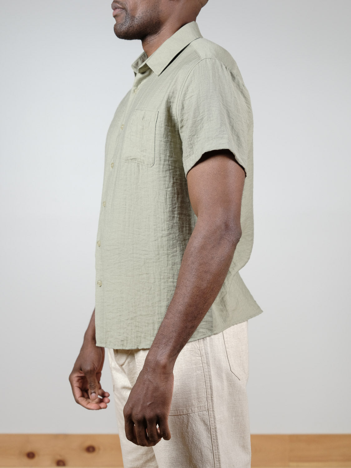 A man in profile wears the ID Menswear Hiker Short Sleeve Shirt in light green with beige pants, standing against a plain background.