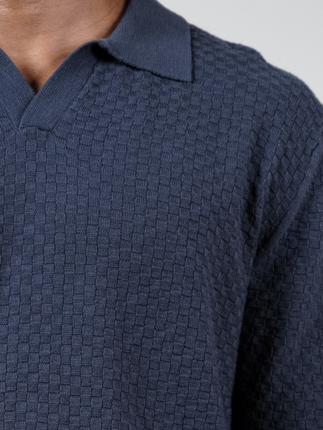 A close-up of a person wearing the ID Menswear Luxor Long Sleeve Cotton Polo in dark blue with a subtle checkerboard texture. The image shows only the shirt and part of the neck and shoulder, highlighting its tailored fit.