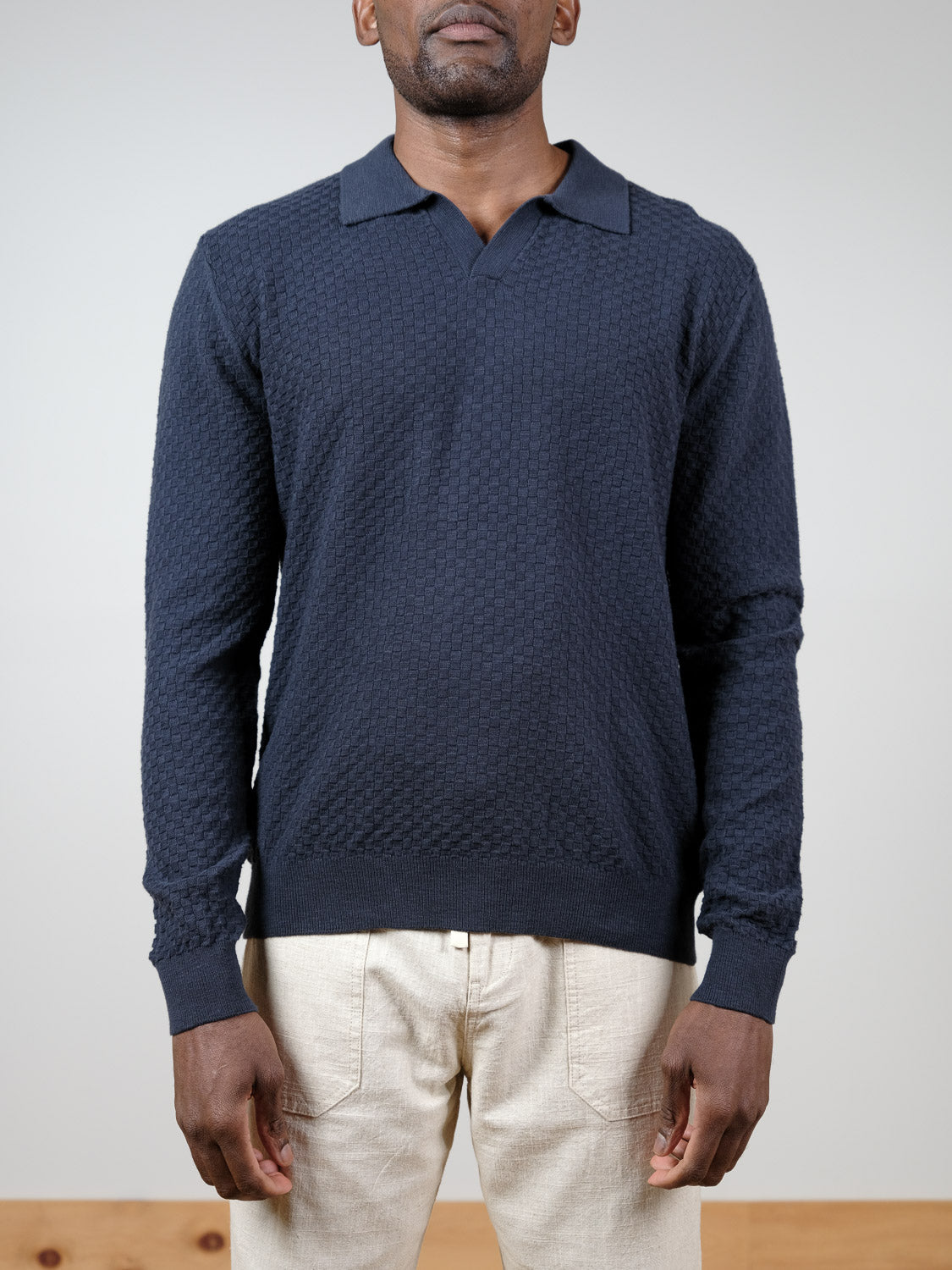 A man stands facing forward against a plain background, wearing an ID Menswear Luxor Long Sleeve Cotton Polo in navy and light beige pants, with his arms relaxed by his sides.