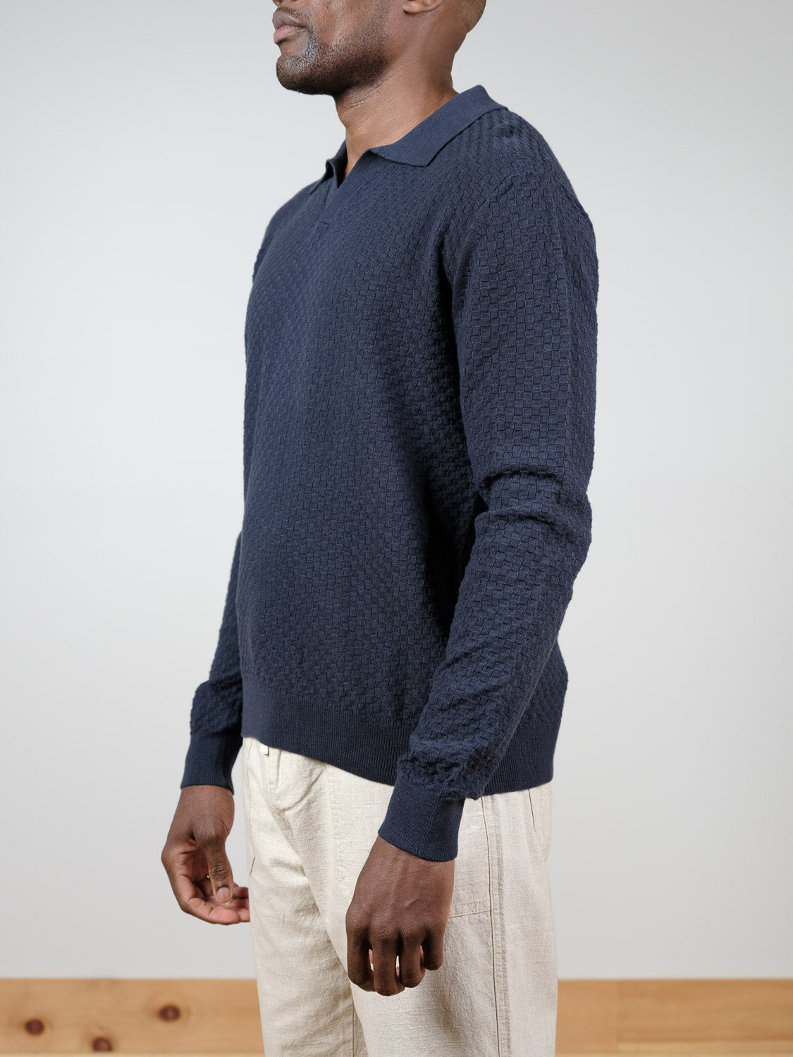 A man stands sideways against a plain background wearing the ID Menswear Luxor Long Sleeve Cotton Polo in navy and light beige pants. His face is partially out of frame.