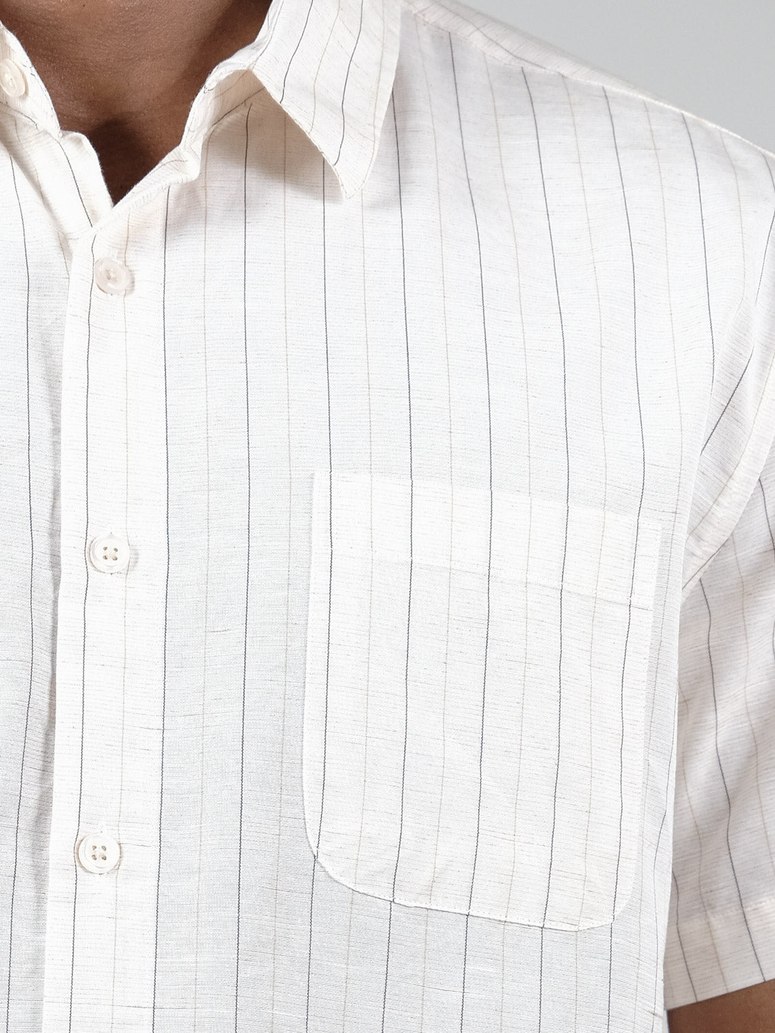 Close-up of a person wearing the Tripper Short Sleeve Shirt by ID Menswear, a white cotton lyocell shirt with thin vertical black stripes, a collar, three buttons, short sleeves, and a left chest pocket.