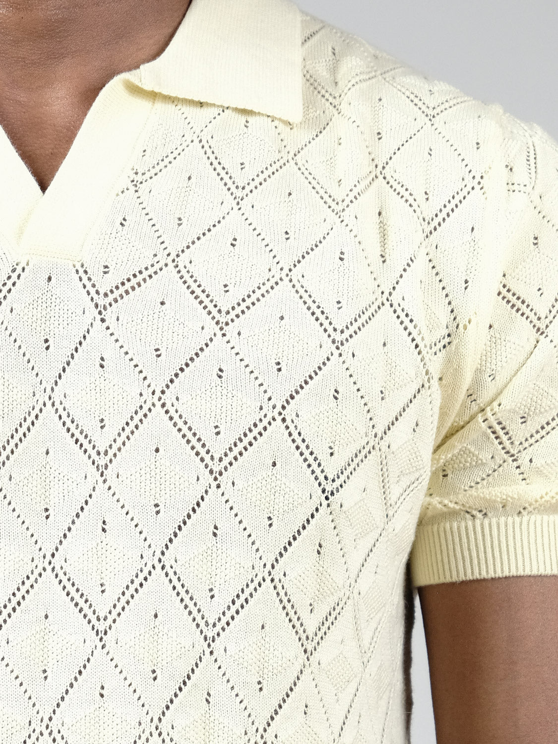 Close-up of a person wearing the Agra Knitted Cotton Polo by ID Menswear, featuring a cream hue, short sleeves, diamond openwork pattern, and ribbed collar—ideal for casual wear.