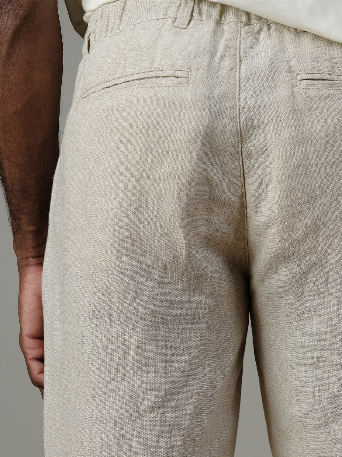 Close-up of a person wearing Casual Friday’s Pandrup Linen Pants in light beige, featuring an elastic waistband and welt back pockets; their left arm is partially visible, showcasing these relaxed summer pants.