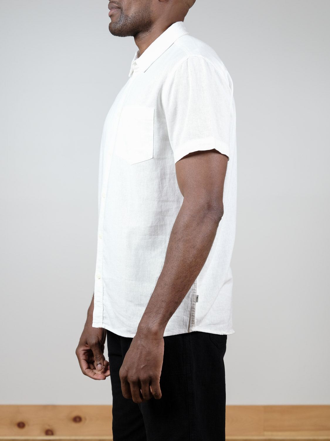 A man stands in profile against a plain background, wearing the !Solid Allan Short Sleeve Shirt—a light-colored, short-sleeve button-up—paired with dark pants.