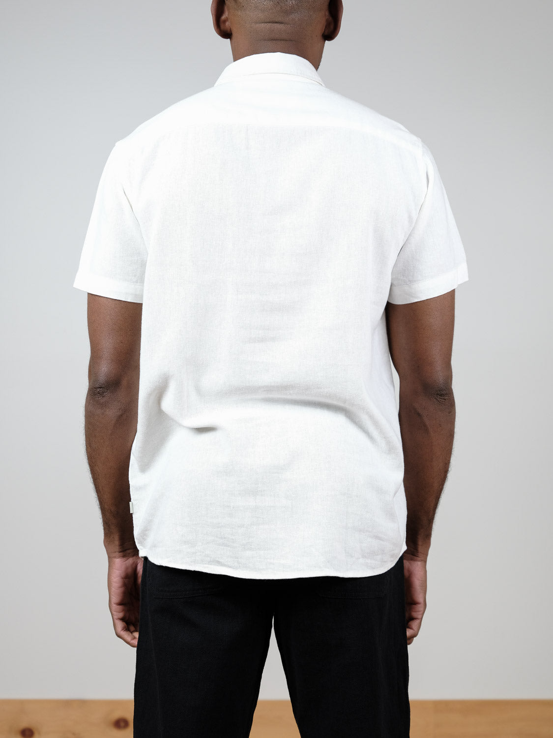 A person faces away from the camera, wearing the !Solid Allan Short Sleeve Shirt and black pants, set against a plain light gray background with a wooden edge at the bottom.