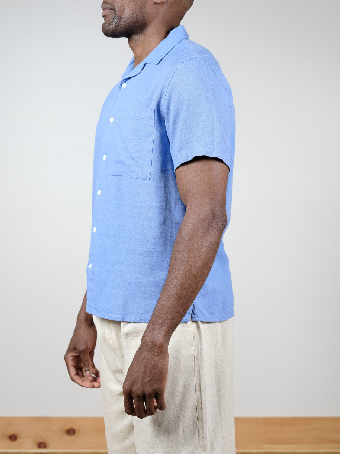 A man stands in profile wearing the !Solid Allan Cuba Woven Short Sleeve Shirt in light blue with a chest pocket and beige pants, set against a plain light background.