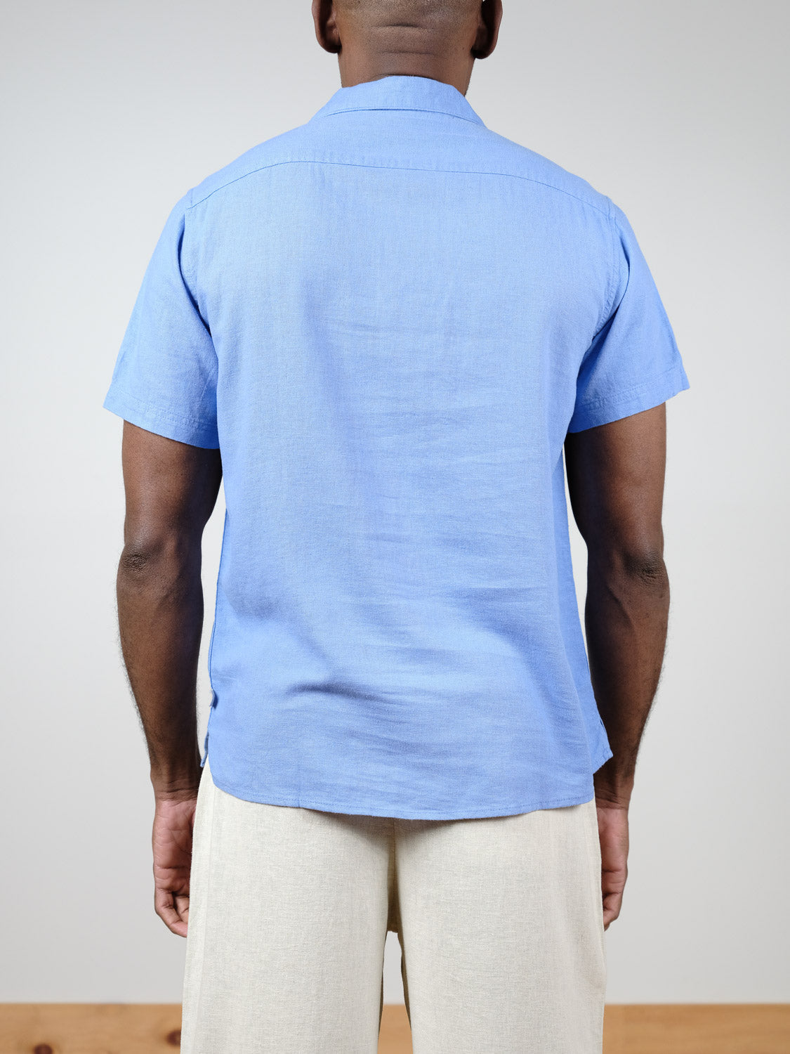A person faces away, wearing the !Solid Allan Cuba Woven Short Sleeve Shirt in light blue with beige pants, set against a plain, light background.