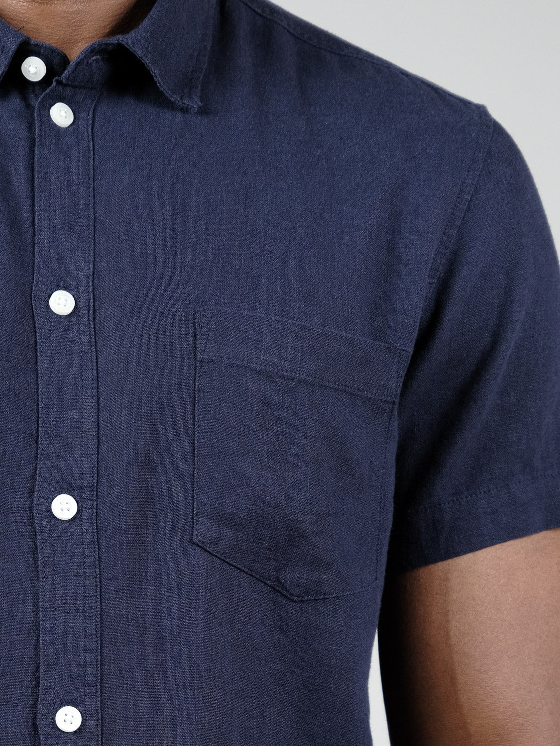 Close-up of a person wearing the !Solid Allan Short Sleeve Shirt in navy blue linen, featuring a chest pocket and white buttons. Only part of the upper torso and arm are visible, showcasing the breathable fabric.