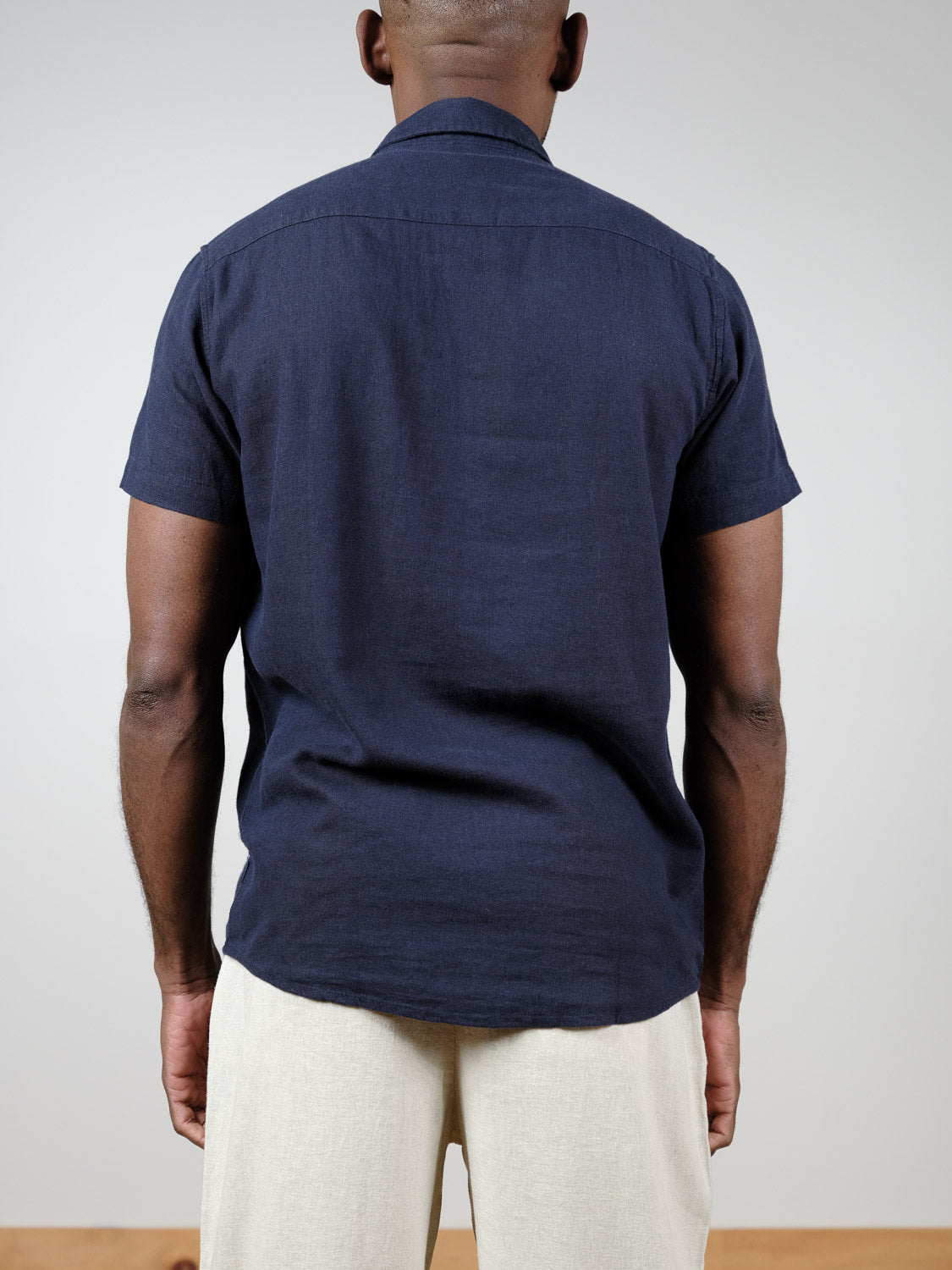 A person faces away from the camera, wearing the !Solid Allan Short Sleeve Shirt in navy blue and light beige pants. Crafted from breathable fabric, this versatile men's shirt offers all-day comfort against a plain background.