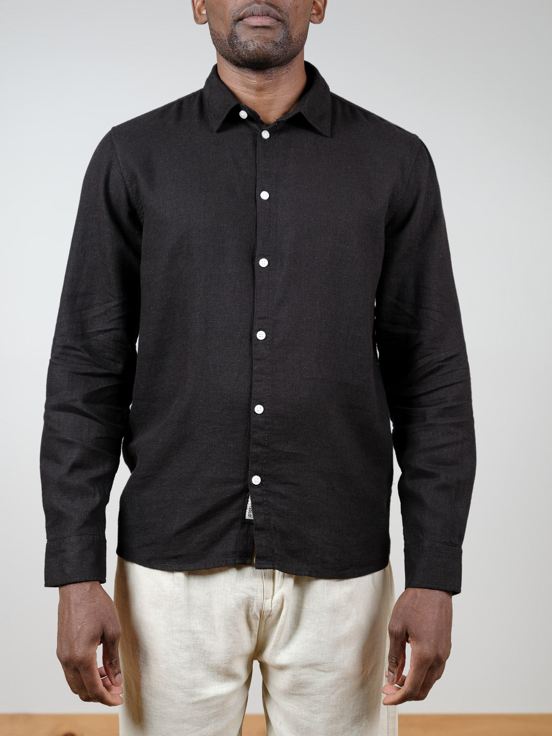 A man wearing the !Solid Enea Allan Long Sleeve Shirt in black and light beige pants stands against a plain, light-colored background.